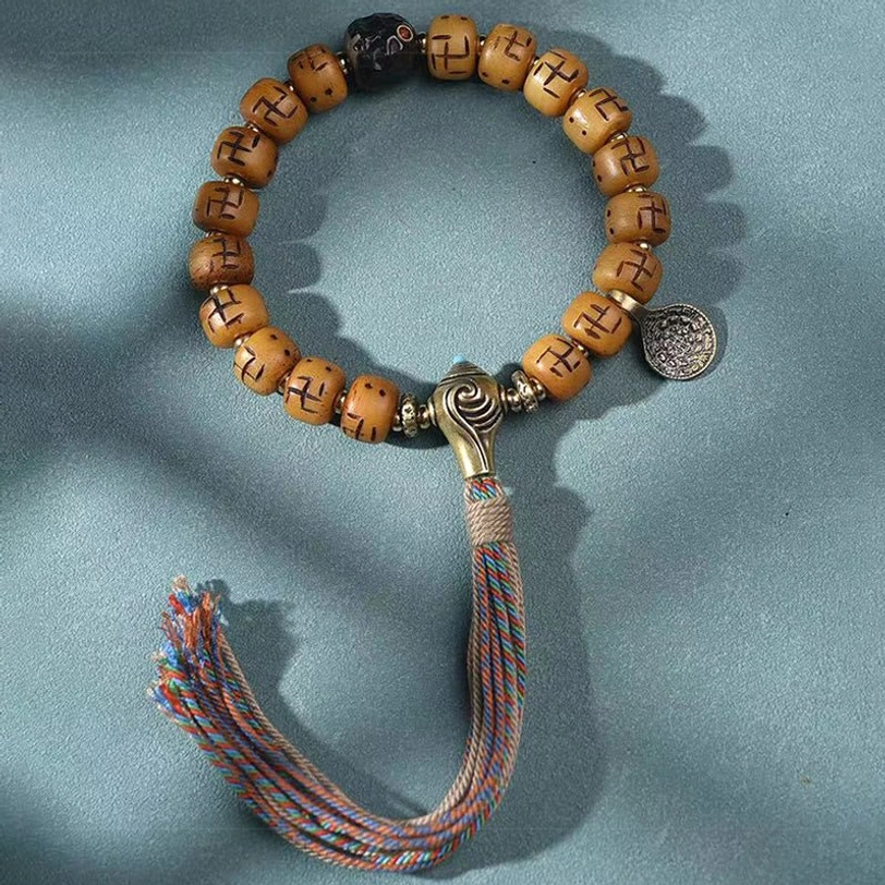 Flat lay of Tibetan bone bead bracelet with faceted black spacers, metal toggle clasp, silver charm, and blue-brown braided tassel detail