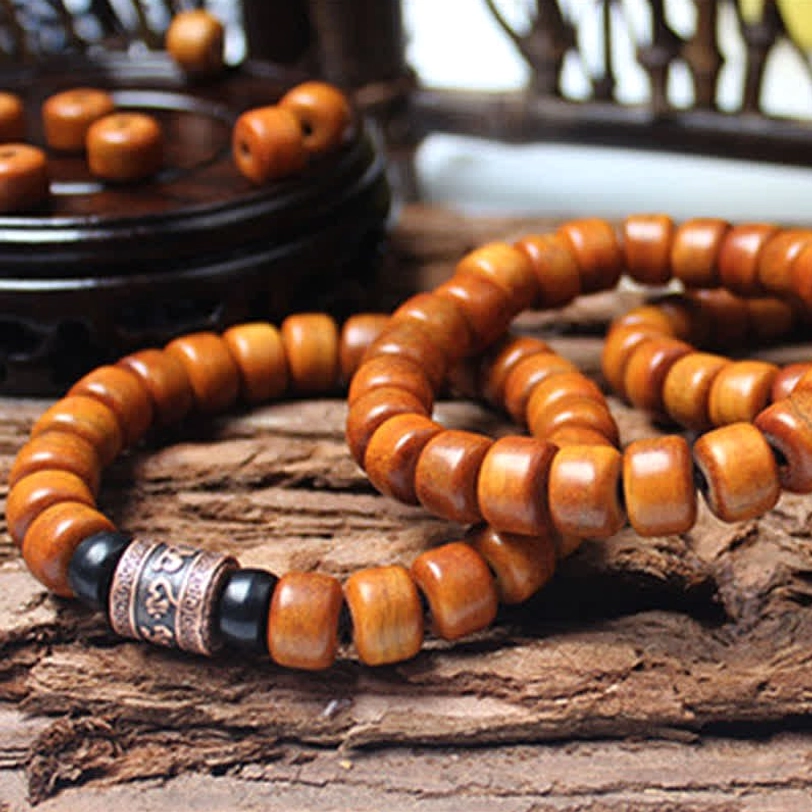 Double-loop Tibetan bone bead bracelet with blue stone spacers and carved metal charm on dark wooden tray