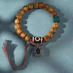 Handmade Tibetan bone bead bracelet featuring carved tan barrel beads, green accent bead, black dzi, and multicolor tassel - flat lay product photography