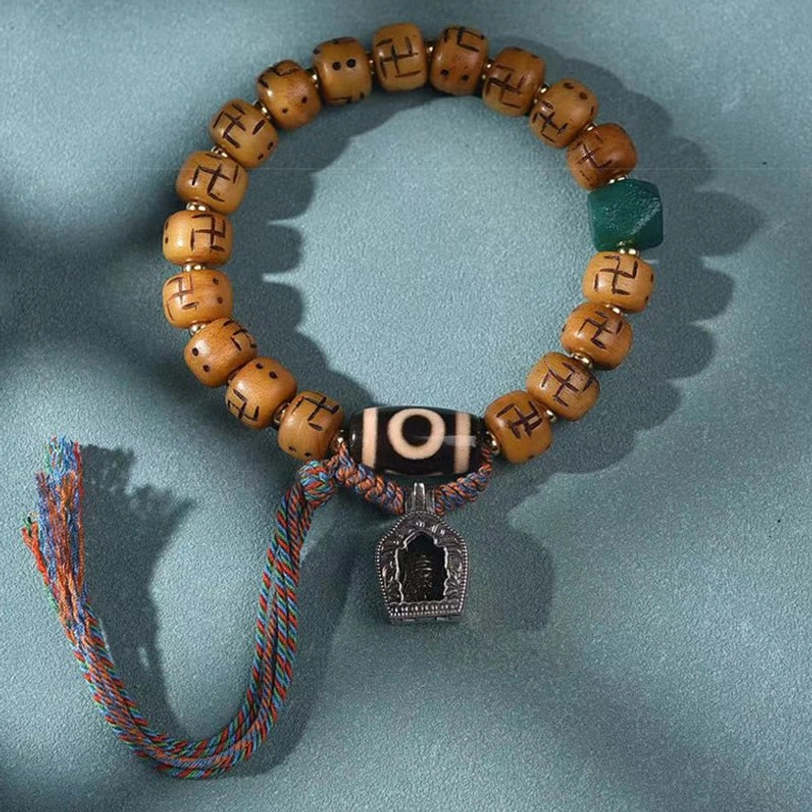 Handmade Tibetan bone bead bracelet featuring carved tan barrel beads, green accent bead, black dzi, and multicolor tassel - flat lay product photography