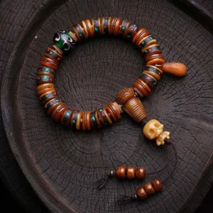 Handmade Tibetan bone bracelet with skull focal bead, decorative trinkets, and drop-shaped pendant on wooden surface