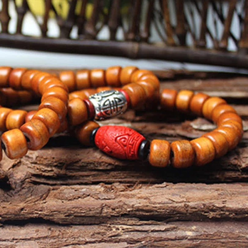 Two Tibetan style beaded bracelets with brown bone beads and decorative red resin accents on wooden background