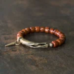 Tibetan bone bead bracelet with antique copper cone pendant, displayed on dark vintage desktop showing side perspective