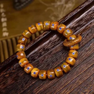 Tibetan bone and lapis lazuli bracelet with copper ring pendant displayed on dark wood surface, showing intricate barrel beads with blue inlay details from above