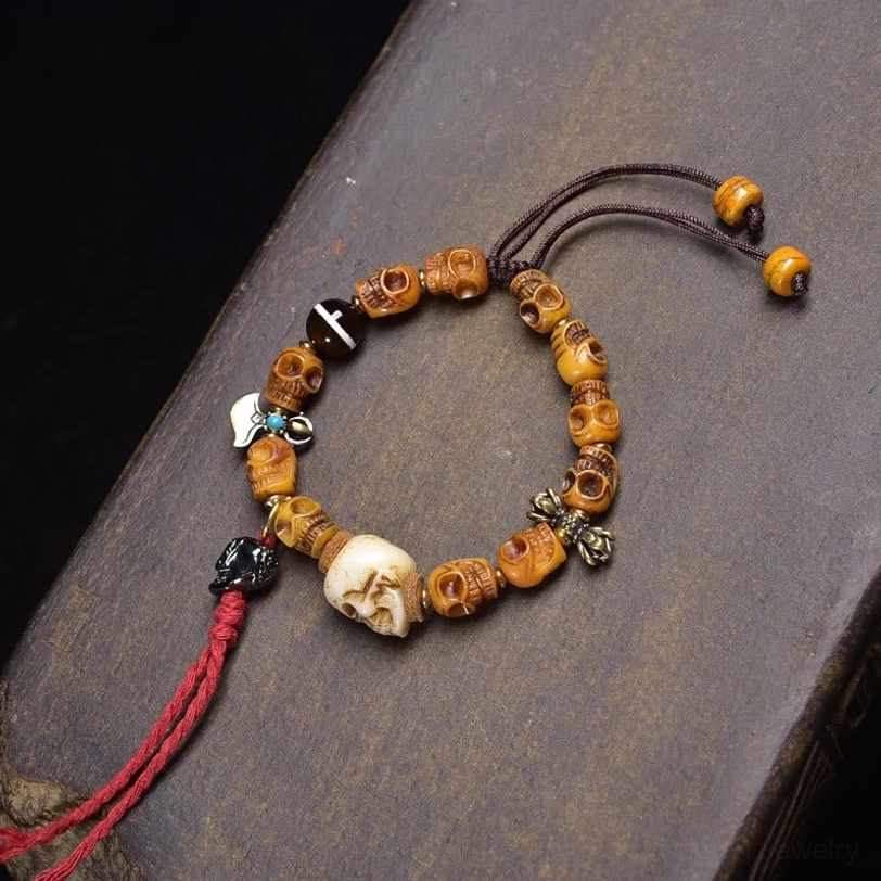 Aged yellow bone skull bracelet with vintage patina and red tassel, adjustable pull-knot closure