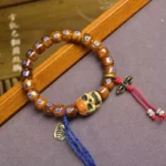 Tibetan bone skull bracelet with blue enamel inlays and red tassel charm, overhead three-quarter view