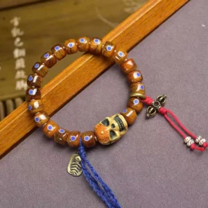 Tibetan bone skull bracelet with blue enamel inlays and red tassel charm, overhead three-quarter view
