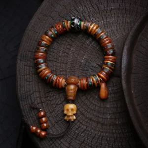 Tibetan bone bead bracelet with carved skull charm, colorful inlaid beads, and metal tassel pendant displayed on dark wooden tray
