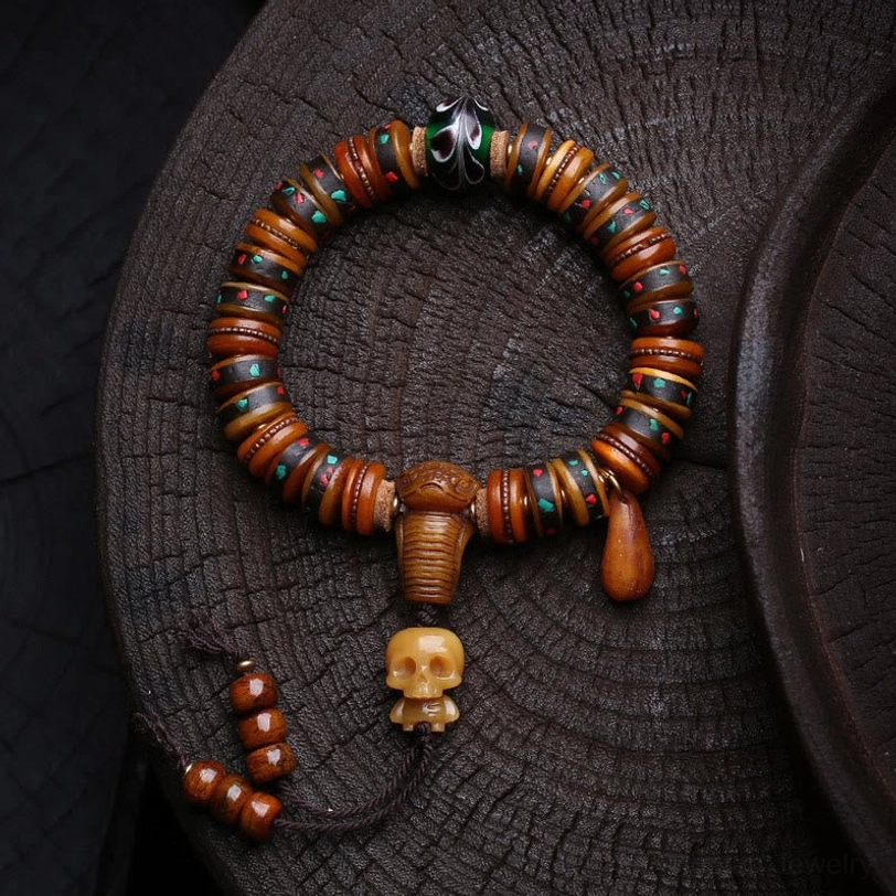 Tibetan bone bead bracelet with carved skull charm, colorful inlaid beads, and metal tassel pendant displayed on dark wooden tray
