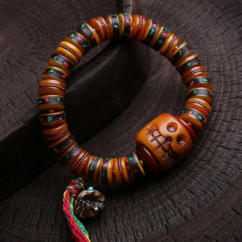 Overhead close-up of Tibetan bone bracelet with carved skull focal bead, inlaid details, and colorful pendant