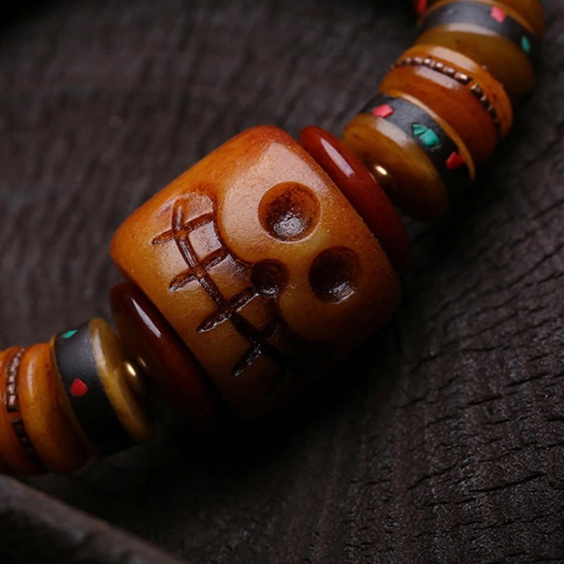 Macro photography of engraved skull pattern on natural bone bead with surrounding colorful inlaid accents