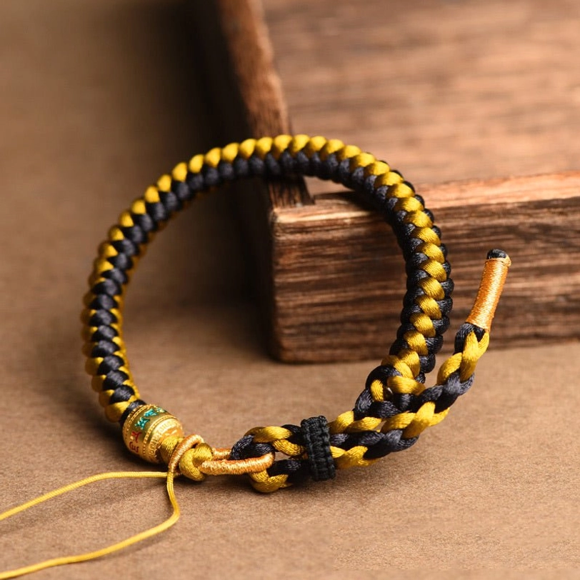 Side view of black gold dragon scale Tibetan bracelet showing adjustable cord and enamel metal charm