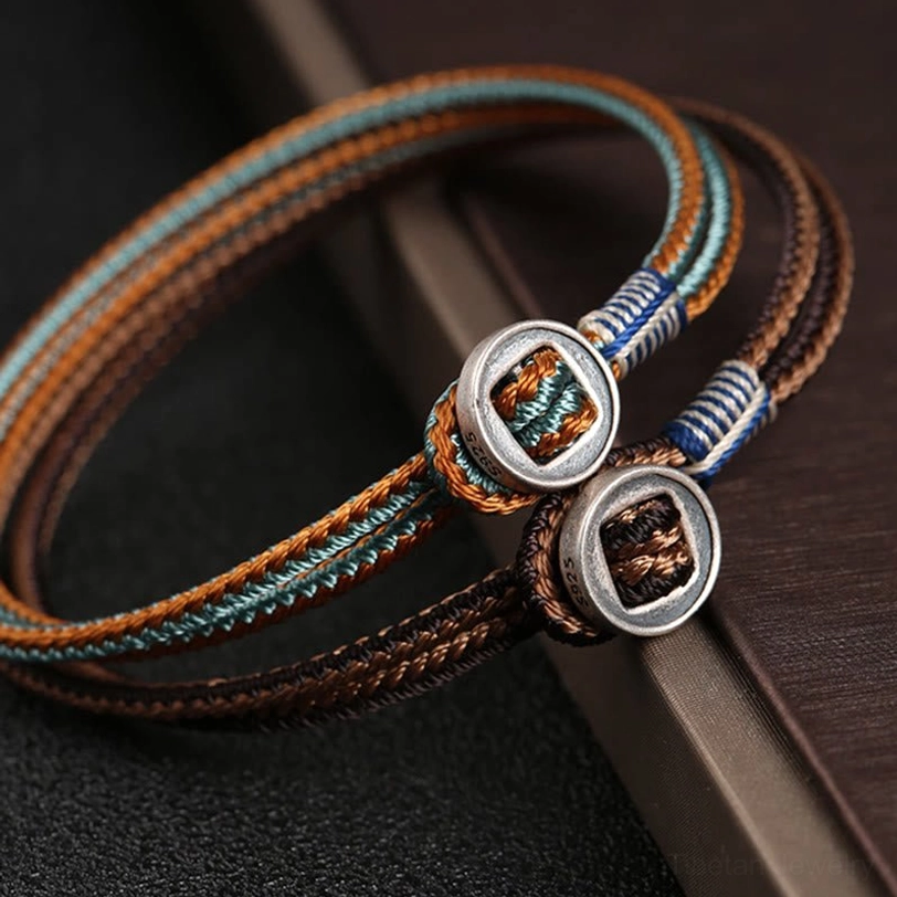 Close-up oblique view of two handwoven tibetan protection bracelets showing detailed braided texture and silver fasteners against dark background