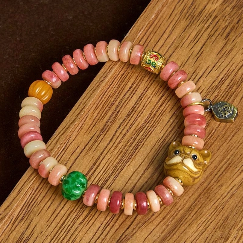 Close-up view of Tibetan camel bone bracelet with warm-toned bone beads, green accent, and carved metal pug head charm on dark wood