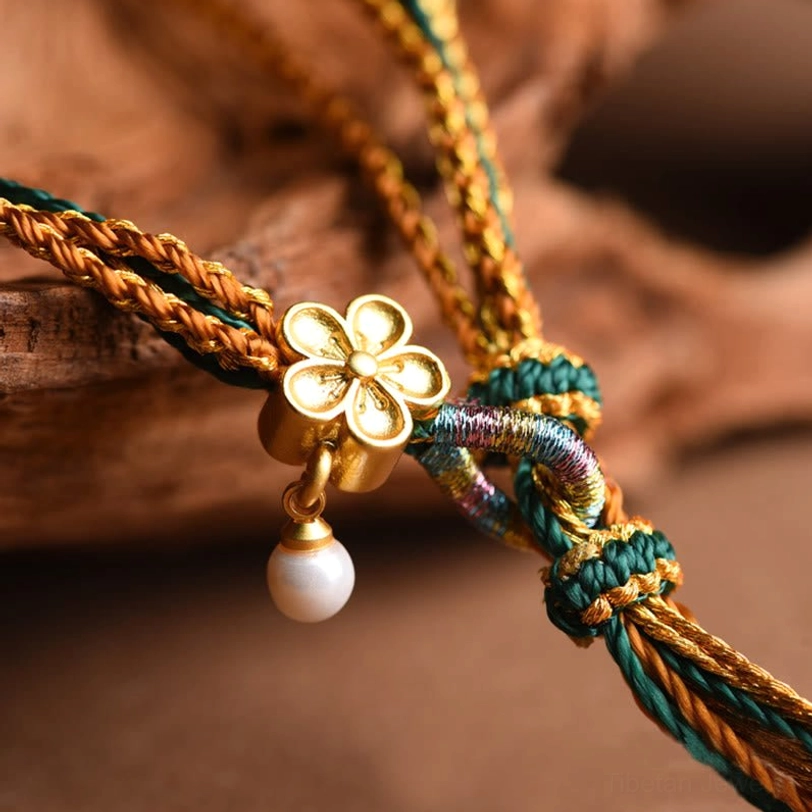 Macro photography of Tibetan bracelet golden flower charm with white pearl pendant and multi-colored woven silk cords on wooden background