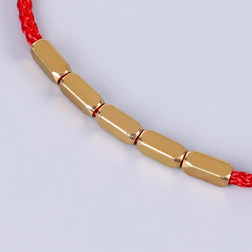 Close-up side view of red Tibetan bracelet showing polished copper barrel beads and woven cord texture