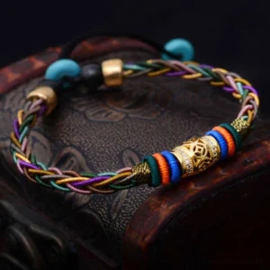 Handmade Tibetan luck bracelet with eight knots and copper charm displayed on carved wooden box, featuring adjustable braided cord and engraved metal accents