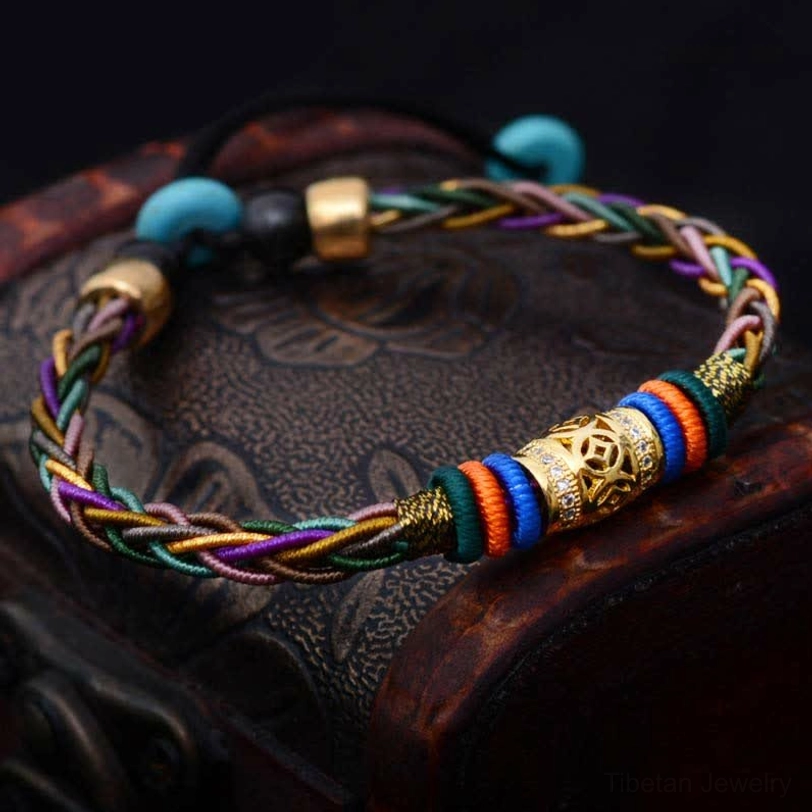 Handmade Tibetan luck bracelet with eight knots and copper charm displayed on carved wooden box, featuring adjustable braided cord and engraved metal accents