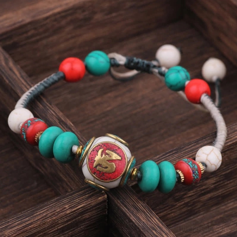 Flat turquoise black white braided rope Tibetan bracelet with script center bead on wooden surface