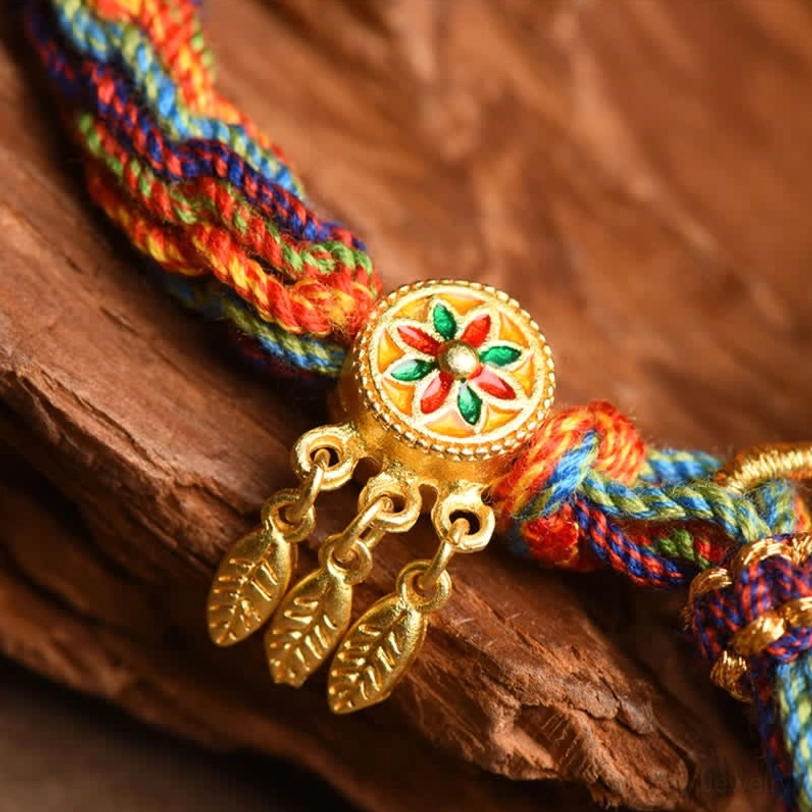Macro close-up of Tibetan bracelet showing enamel flower pendant, gold leaf charms, and twisted multicolor rope detail