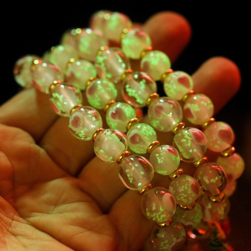 Hand holding Tibetan bracelet with green fluorescent glass beads showing glow-in-the-dark effect