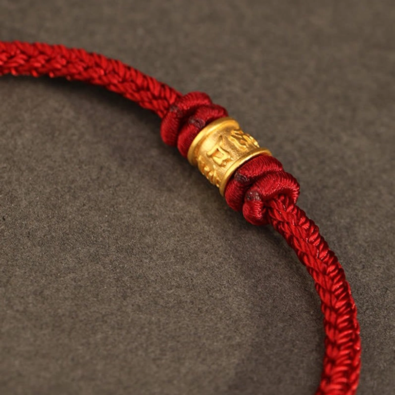 Close-up detail of Om Mani Padme Hum gold charm with braided red cord knots, handcrafted Tibetan bracelet