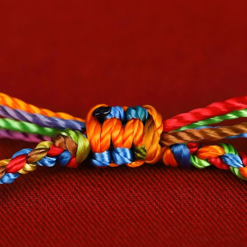Intricate hand-tied knot detail of multicolored Tibetan wish bracelet showing rainbow mixed threads on red velvet