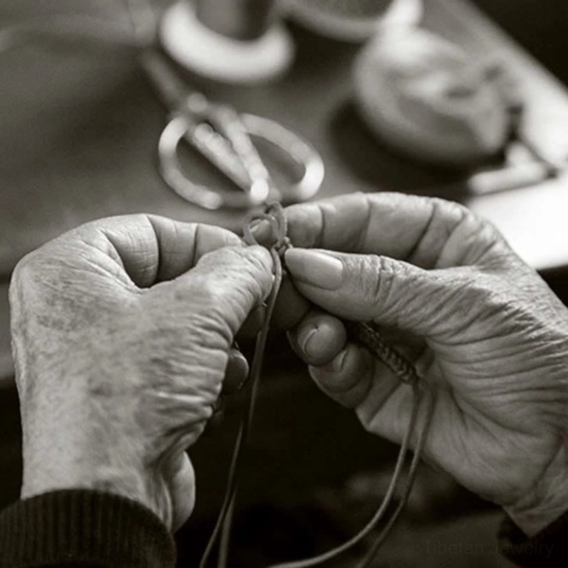 Handmade Tibetan blessing bracelet being woven by artisan hands in traditional workshop setting
