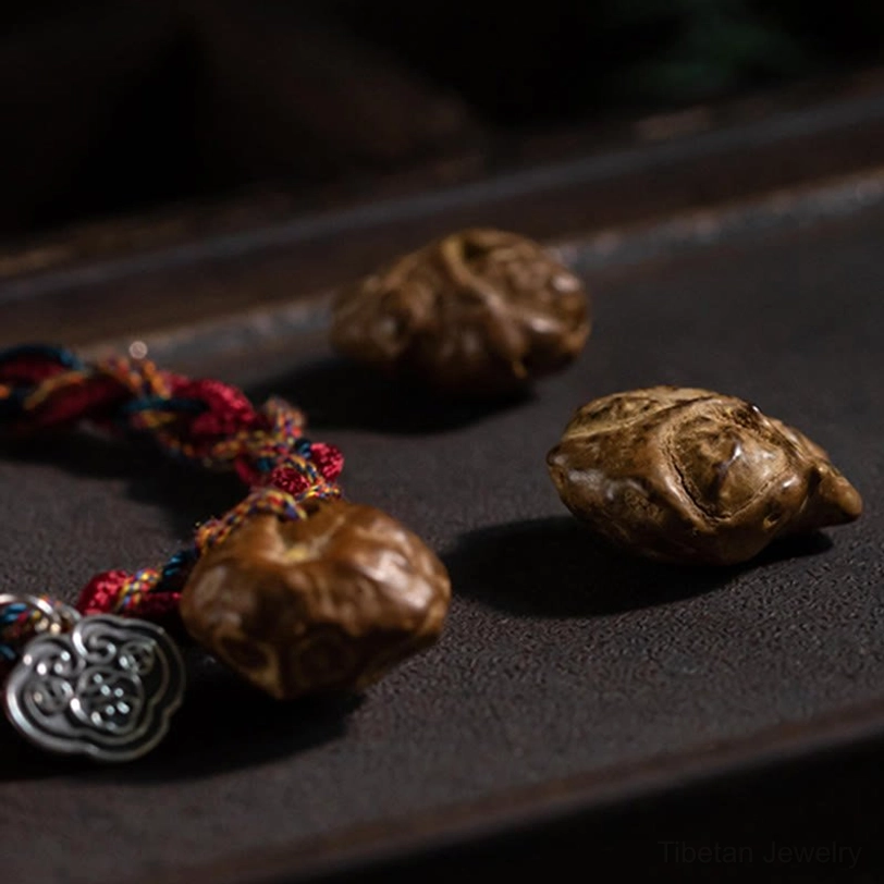 Macro close-up of Tibetan bracelet showing silver ruyi charm, carved wooden bead, and twisted red cord texture detail