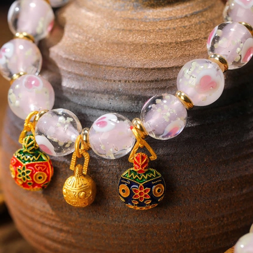 Macro close-up of Tibetan bracelet showing detailed luminous pink glass beads with gold beast guardian charm