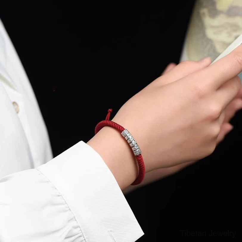 On-model wrist shot of red Tibetan Om Mani Padme Hum rope bracelet worn on left wrist with silver charm visible