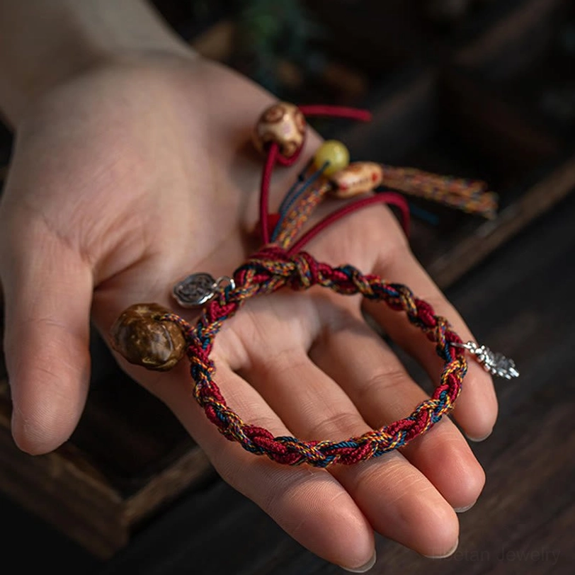 Handmade Tibetan bracelet held in palm showing silver leaf charm and mixed natural beads on wooden surface