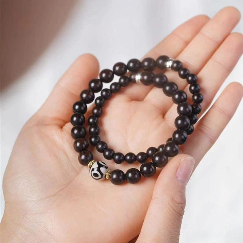 Double wrap ebony wood dzi bead bracelet in palm, showing traditional tibetan design with protective dzi bead centerpiece