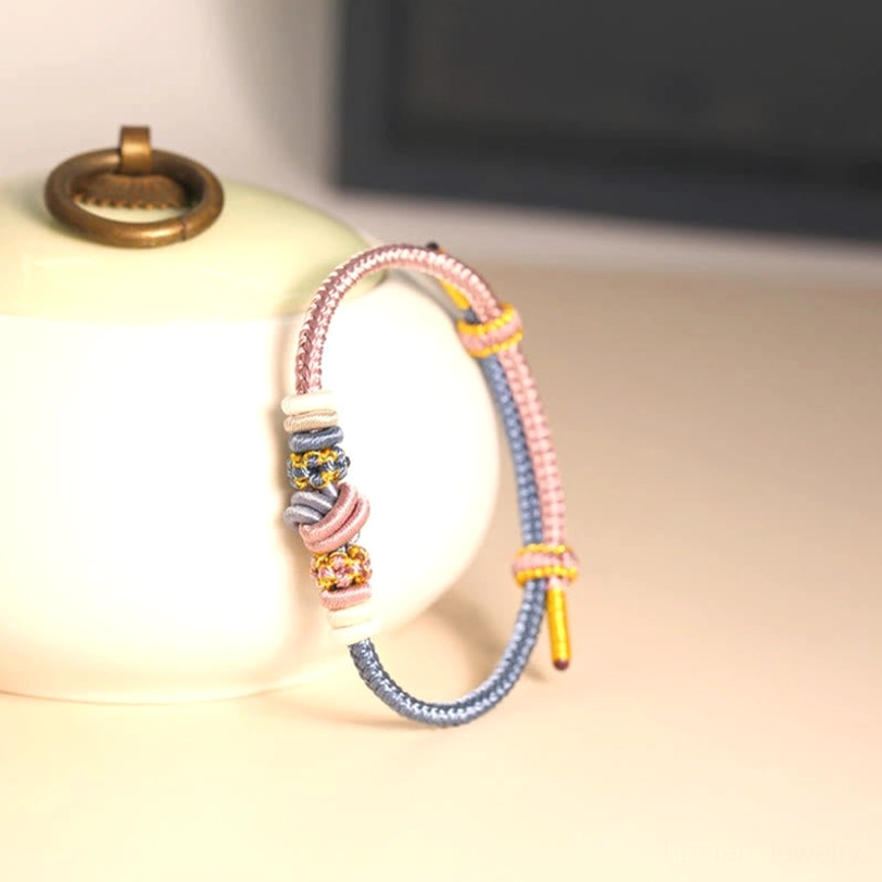 Delicate pink and blue Tibetan braided bracelet displayed on natural ceramic background showing eight-thread sacred knot