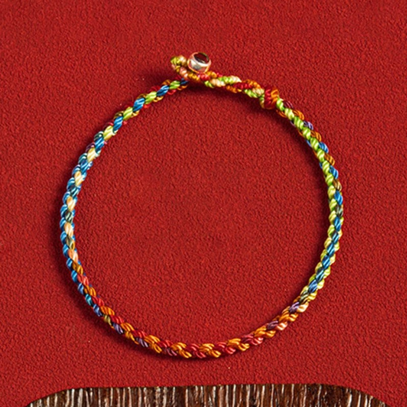 Close-up of woven Tibetan multicolor threads showing rainbow gradient and silver toggle fastener