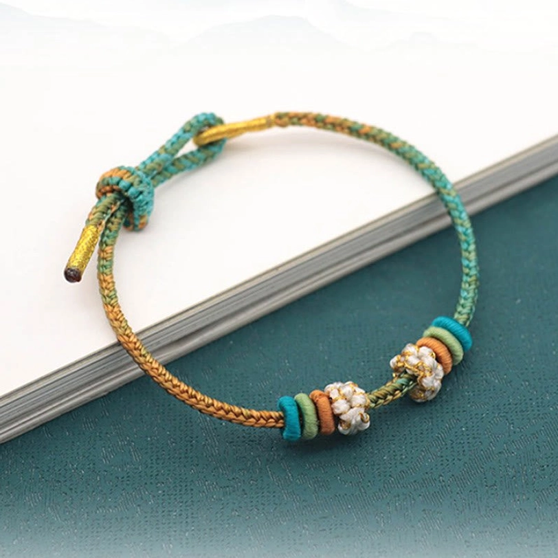 Braided peace knot lucky rope bracelet featuring teal and bronze woven threads with decorative flower beads on dark surface