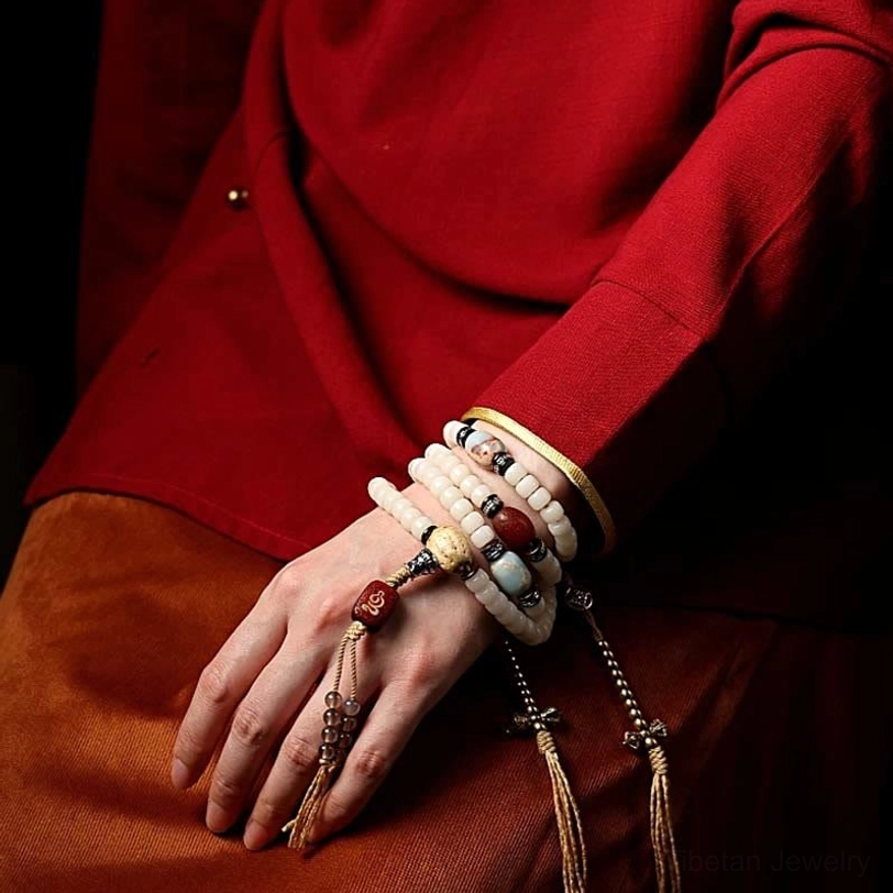 Layered tibetan style bracelets with white bodhi beads and silver vajra tassel pendant worn on hand with traditional clothing