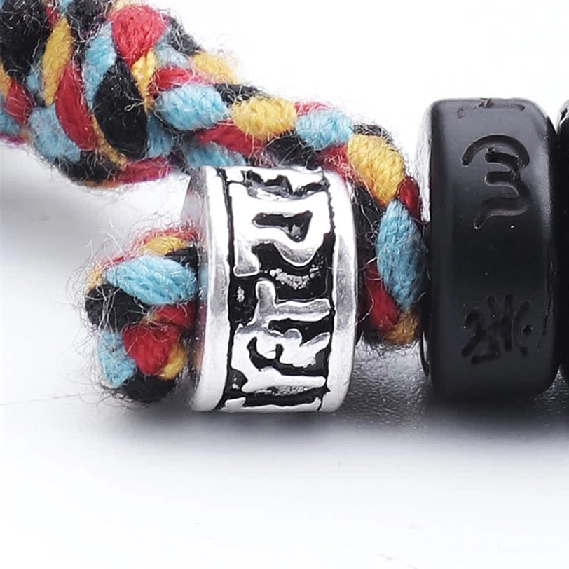 Tibetan bracelet fastener macro close-up showing colorful woven tassel cord, silver engraved charm bead, and black coconut shell mantra bead