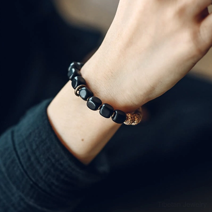 Worn Tibetan protection bracelet on wrist close-up showing black round beads and metal components with dark green outfit styling