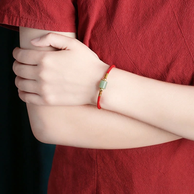 Tibetan protection bracelet worn on wrist showing red braided rope with green gemstone, styled with casual outfit