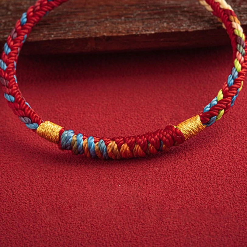 Multicolor woven Tibetan blessing bracelet with gold thread wraps, low angle view on red background with wooden accents