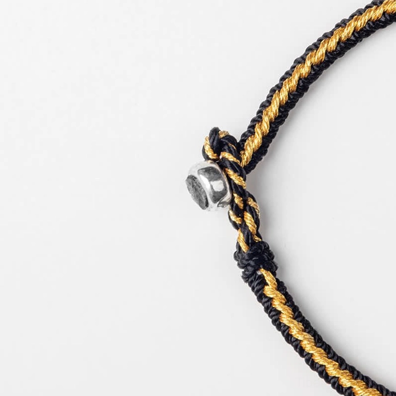 Close-up macro detail of Tibetan braided protection bracelet showing black and gold twisted rope texture and silver clasp