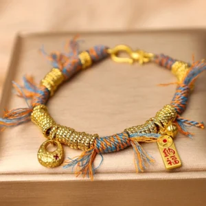 Handmade Tibetan multicolor braided rope bracelet with gold charm pendant on satin jewelry tray, featuring blue and orange woven cord with blessing tag