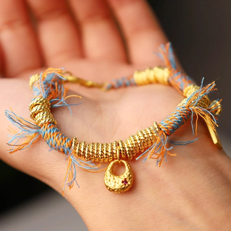 Tibetan multicolor woven bracelet resting on palm, displaying full braided design with gold round pendant and blue-orange tassel fringe