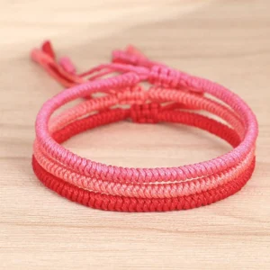 Top-down view of 3-piece Tibetan braided protection bracelet set showing ombre red layered woven structure on wooden surface