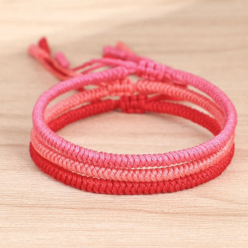 Top-down view of 3-piece Tibetan braided protection bracelet set showing ombre red layered woven structure on wooden surface