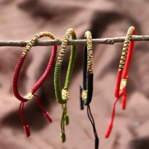 Multiple Tibetan braided friendship bracelets in various color combinations hanging on natural wood twig, showing King Kong knot design