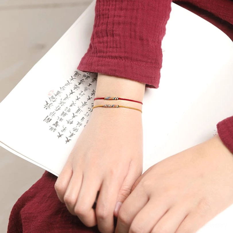 Stacked thin woven Tibetan bracelets in red and yellow on arm with calligraphy background showing minimalist style