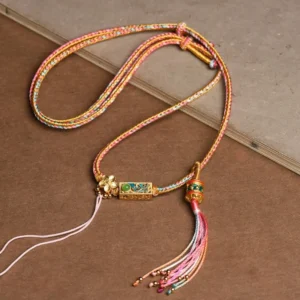 Tibetan colorful braided string copper prosperity necklace with pink tassel and gold charm pendant on desktop display