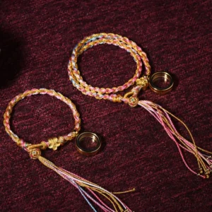 Two Tibetan braided lucky bracelets with gold accents and long tassels on red velvet fabric, flat lay top view